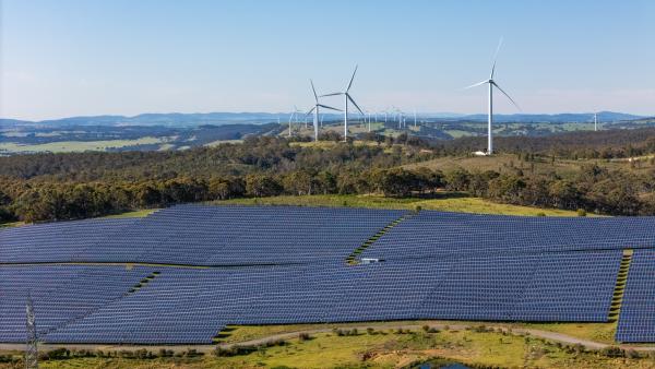 Drone shot of a field of solar panels with wind turbines in the distant background